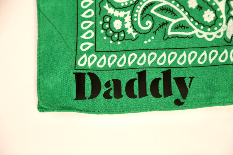 May include: Green bandana with a white paisley pattern and the word "Daddy" printed in black.