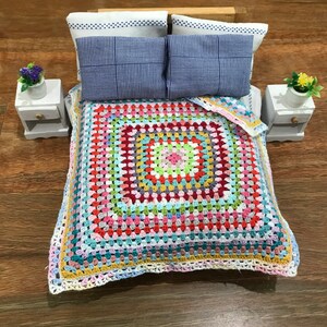 May include: A colourful crocheted bedspread with a square pattern in shades of pink, green, blue, yellow, and red. The bedspread is on a wooden bed frame with two blue and white striped pillows.