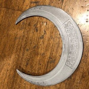 May include: A silver crescent moon-shaped metal object with the words "All That Glitters Is Not Gold" engraved on the outside.