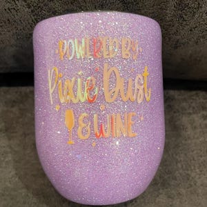 Może przedstawiać: Fioletowy kubek do wina z brokatem z napisem "Powered by Pixie Dust & Wine" w kolorowej czcionce.