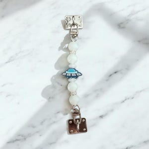 May include: A white beaded keychain with a silver clasp and a blue and white UFO charm.