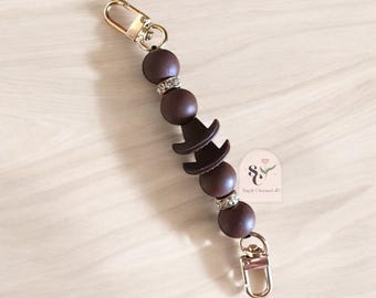 May include: A brown and gold charm necklace with a hat charm and rhinestones. The necklace is made of silicone beads and has a gold lobster clasp.