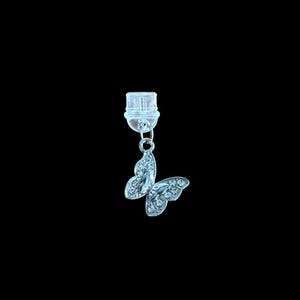 May include: A silver butterfly charm with clear crystals hangs from a clear plastic clasp. The butterfly has detailed wings and is set against a black background. This jewelry item is suitable for necklaces or bracelets.