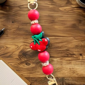 May include: A red and green cherry charm with rhinestones on a gold chain with two clasps.