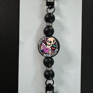 May include: A black beaded keychain with a "Spooky Book Club" charm. The charm features a skull reading a book, surrounded by bats and stars. The keychain has silver-tone hardware.