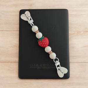 May include: White and red beaded keychain with a strawberry charm and a silver heart-shaped clip.