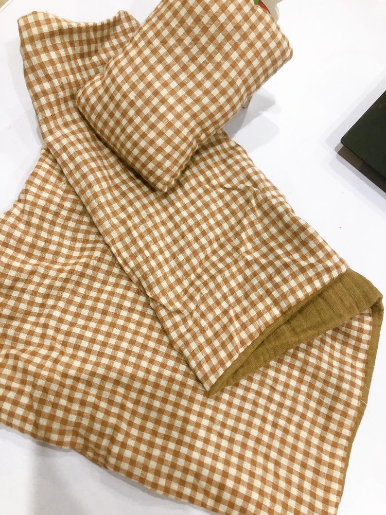 K&ouml;nnte beinhalten: Eine braune und wei&szlig;e Gingham-Babydecke mit einem braunen und wei&szlig;en Gingham-Kissen. Die Decke hat auf einer Seite eine weiche, flauschige Textur.