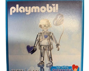 May include: Playmobil box featuring a clear figure holding a heart-shaped balloon and a heart. The figure has a blue heart on its chest and a blue heart in its hand. The box has the Playmobil logo and the text "WE LOVE PLAYMOBIL".