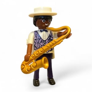 Puede incluir: Una figura de Playmobil de un músico de jazz tocando un saxofón dorado. La figura lleva un sombrero blanco, una camisa blanca, un chaleco estampado y pantalones morados oscuros. El saxofón se sostiene con ambas manos.