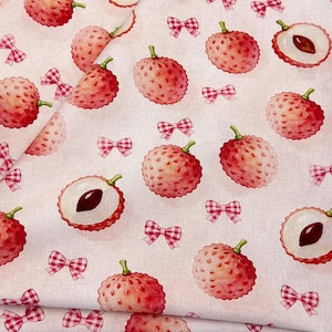 Könnte beinhalten: Ein hellrosa Stoff mit einem sich wiederholenden Muster aus ganzen und halbierten Litschis in Rot- und Weißtönen, durchsetzt mit kleinen, rosa-weiß karierten Schleifen, die über die Oberfläche des Textilmaterials verteilt sind.