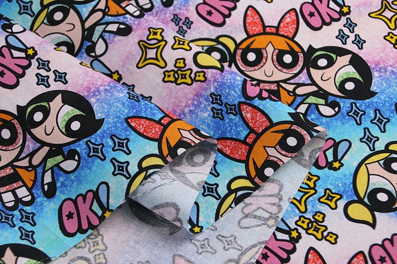 Puede incluir: Una tela colorida con un patr&oacute;n repetitivo de chicas de dibujos animados con ojos grandes y la palabra "OK" en rosa, azul y amarillo. El fondo es un patr&oacute;n de brillo azul y rosa.