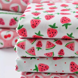 Puede incluir: Una pila de tela blanca doblada con un patr&oacute;n repetido de fresas rojas y rodajas de sand&iacute;a. Las fresas tienen tallos verdes y semillas negras. Tambi&eacute;n se ve tela adicional con un patr&oacute;n de cerezas rosas.