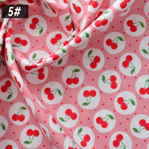 Puede incluir: Tela rosa con un patr&oacute;n repetido de cerezas rojas dentro de c&iacute;rculos blancos y peque&ntilde;os puntos rojos. El n&uacute;mero "5#" est&aacute; en la esquina superior izquierda. La tela est&aacute; doblada, creando sombras y profundidad.