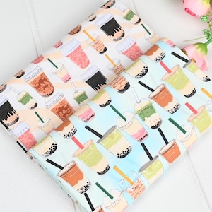 May include: Two fabric pieces featuring a repeating pattern of bubble tea drinks in various colours. The drinks include brown, pink, green, and black, with straws and lids. The background is light blue and white.