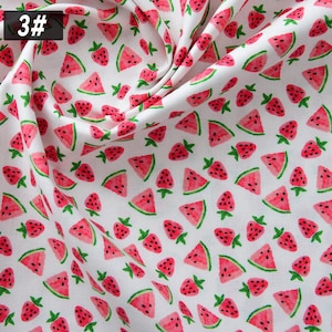 Puede incluir: Tela blanca con un patr&oacute;n repetido de rodajas de sand&iacute;a rojas y fresas con tallos verdes. La tela tiene un aspecto suave y fluido. El n&uacute;mero "3#" est&aacute; en la esquina superior izquierda.