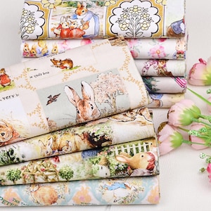 Op de afbeelding: Een stapel stof met illustraties van Peter Rabbit en andere personages. De stof heeft een crèmekleurige achtergrond met kleurrijke afbeeldingen van konijnen, bloemen en scènes uit de kinderboekenserie.