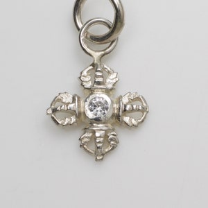 Peut inclure: Charme en argent avec un cristal transparent au centre et un motif à quatre pointes. Le charme a une boucle en haut pour l'attacher à un collier ou un bracelet.
