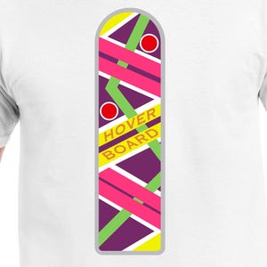 Pode incluir: Camiseta branca com um gráfico de um hoverboard do filme De Volta para o Futuro. O hoverboard é amarelo, roxo, verde e rosa com círculos vermelhos na lateral. O texto "Hoverboard" está impresso em laranja no gráfico.
