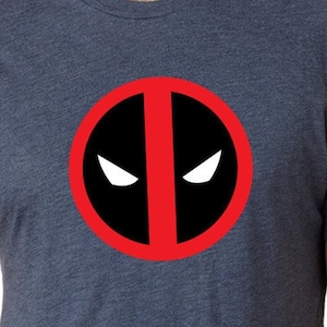 May include: A dark blue t-shirt with a red circle and a black Deadpool mask inside. The mask has white eyes.