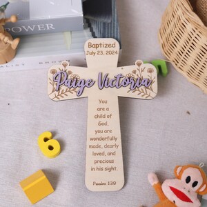 Könnte beinhalten: Ein Holzkreuz mit dem Namen "Paige Victoria" in lila Schrift, floralen Akzenten und dem Datum "23. Juli 2024". Das Kreuz enthält ein religiöses Zitat aus Psalm 139. Ein Taufgeschenk.