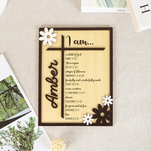 May include: Wooden framed sign with the name "Amber" in a cursive font. The sign features a cross design and the words "I am..." followed by a list of affirmations. Decorative daisy cutouts are placed on the frame.