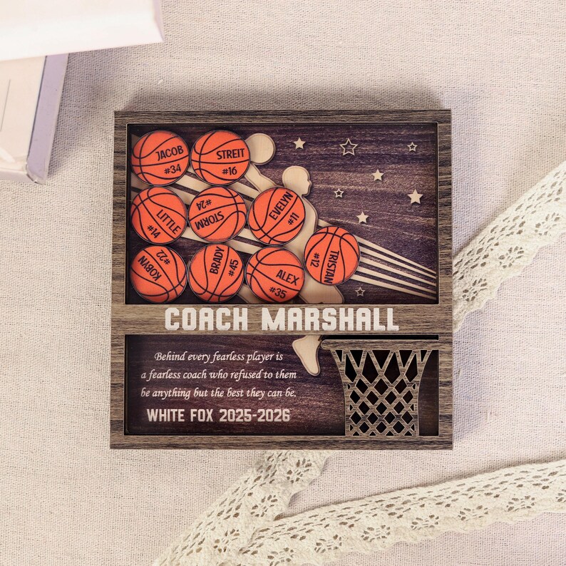May include: Wooden basketball-themed plaque with a dark wood frame. Features basketballs with player names and numbers, a basketball net, and the text "COACH MARSHALL". Includes the text "WHITE FOX 2025-2026".