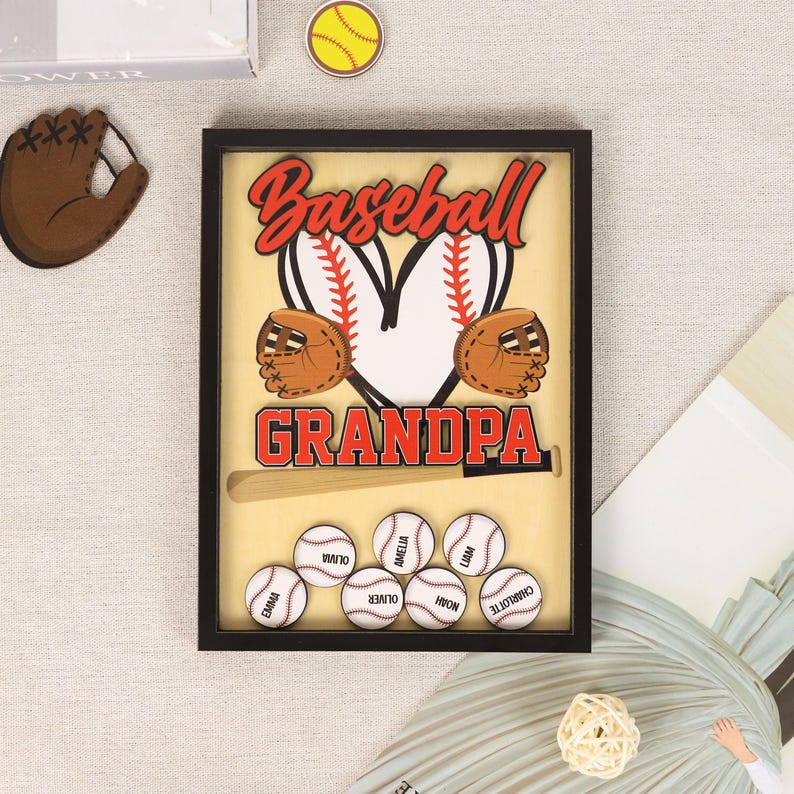 Peut inclure: Un souvenir sur le th&egrave;me du baseball encadr&eacute; avec le mot "Baseball" en script rouge au-dessus de "Grandpa". Le design comprend une balle de baseball, des gants et des balles de baseball avec des noms. Le cadre est noir.