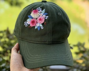 May include: A dark green baseball cap with a floral embroidery design featuring pink and white roses and green leaves.