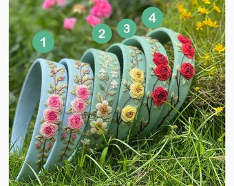 May include: Five light blue headbands with embroidered floral designs. The headbands feature different floral patterns, including pink roses, yellow flowers, and red roses.
