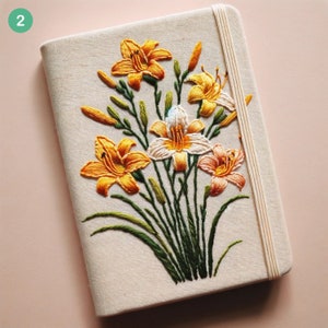 Può includere: Un taccuino di lino bianco con un ricamo floreale. I fiori sono gialli, arancioni e bianchi e sono disposti a mazzo. Il taccuino ha una chiusura a nastro bianco.