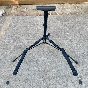 Puede incluir: Un soporte de guitarra de metal negro con base de tr&iacute;pode y brazos de apoyo acolchados con espuma. El poste vertical central cuenta con un reposacabezas en forma de T y un peque&ntilde;o logotipo amarillo de Fender en el eje central.