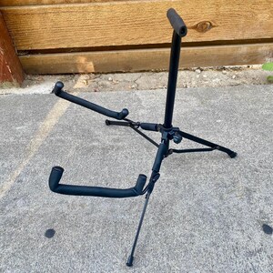 Puede incluir: Un soporte de guitarra de metal negro con una base de tr&iacute;pode de tres patas, un poste de soporte vertical con un apoyo superior y dos brazos inferiores. Todos los puntos de contacto est&aacute;n cubiertos con espuma negra para proteger el instrumento.