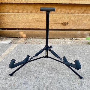 Puede incluir: Un soporte de guitarra de metal negro con un poste de soporte vertical con una parte superior en forma de T y dos brazos de base en &aacute;ngulo. El soporte incluye acolchado de espuma en todos los puntos de contacto y muestra el logo Fender en dorado.