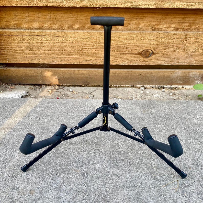 Puede incluir: Un soporte de guitarra de metal negro con un poste de soporte vertical con una parte superior en forma de T y dos brazos de base en &aacute;ngulo. El soporte incluye acolchado de espuma en todos los puntos de contacto y muestra el logo Fender en dorado.