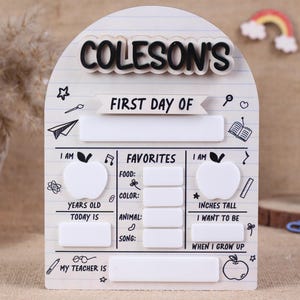 May include: A white arched wooden sign with a lined paper pattern featuring the text "COLESON'S FIRST DAY OF" and blank spaces for filling in details like age, height, favorites, and teacher's name, decorated with black line art school icons.