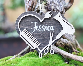 May include: A wooden heart-shaped ornament with a comb, scissors, and hair dryer design. The ornament is personalized with the name "Jessica".