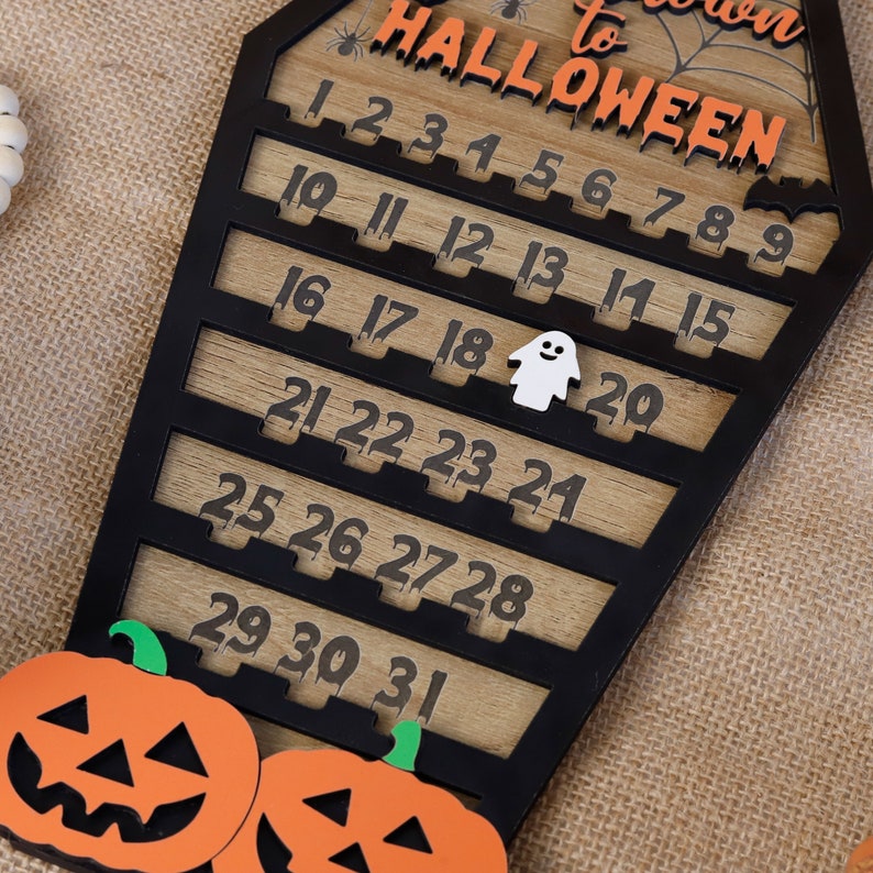 May include: A wooden countdown calendar shaped like a coffin with the text "Countdown to Halloween" and numbers 1 through 31. The calendar is decorated with a spider web, a spider, and a ghost.