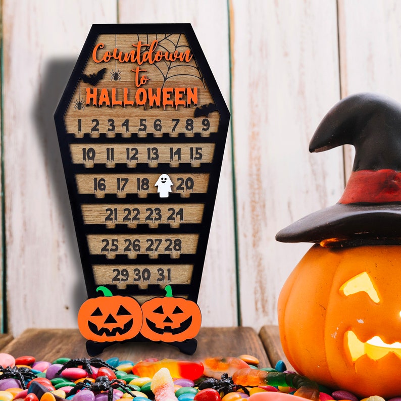 May include: Wooden countdown calendar shaped like a coffin with the text "Countdown to Halloween" and numbers 1 through 31. The calendar is decorated with bats, spiders, and a ghost. There are two pumpkins at the bottom of the calendar.
