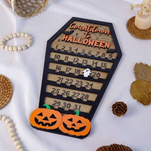 May include: A wooden Halloween countdown calendar shaped like a coffin with a black and orange color scheme. The calendar has numbers 1 through 31, with a ghost and pumpkins at the bottom.