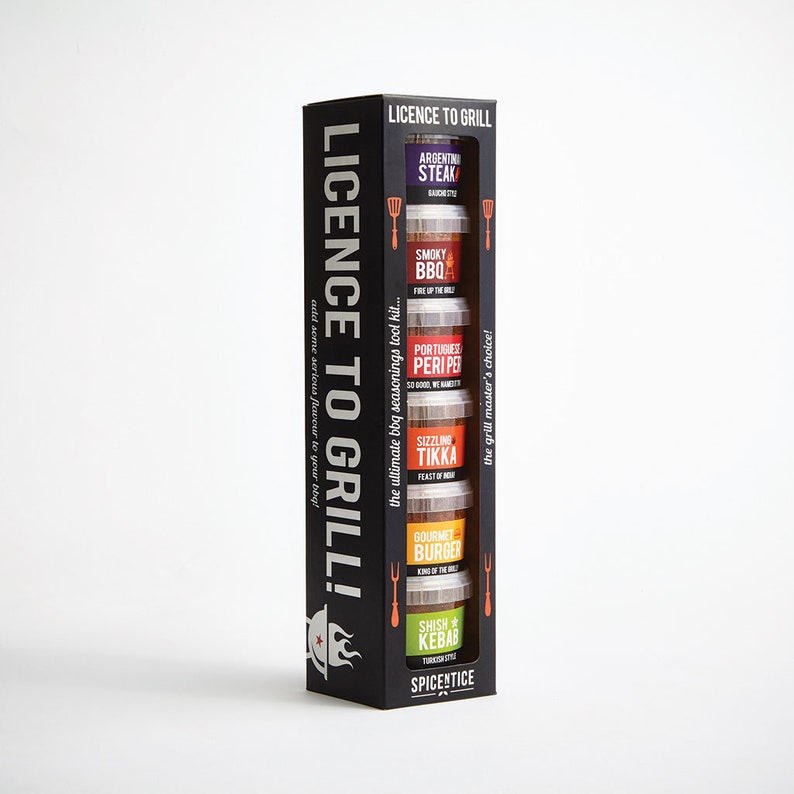 May include: A black box with a clear window showing five small jars of spices. The jars are labeled with different flavors, including Argentinian Steak, Smoky BBQ, Portuguese Peri Peri, Sizzling Tikka, Gourmet Burger, and Shish Kebab. The box is labeled "Licence to Grill!" and "The grill master's choice!"