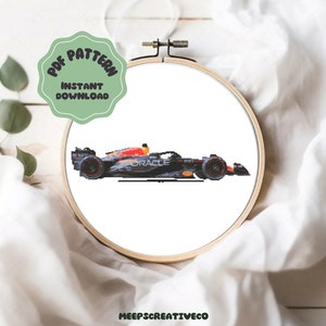 Peut inclure: Une voiture de course de Formule 1 noire et rouge avec le mot "Oracle" sur le côté. La voiture est dans un cerceau de broderie blanc.