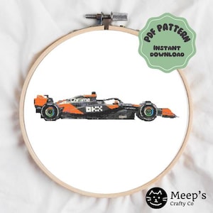 May include: A cross-stitch pattern of a black and orange Formula 1 race car with the word "Chrome" on the side. The pattern is in a white embroidery hoop.