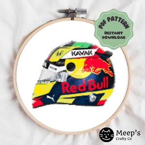Può includere: Uno schema di punto croce con un casco da corsa colorato con le parole "Red Bull" e "KAVAK" su di esso.