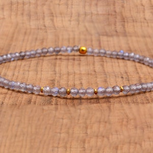 May include: A delicate bracelet made with small, iridescent gray beads and gold accents.