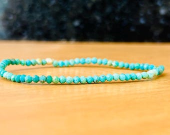 May include: A turquoise gemstone bracelet with small, faceted beads. The bracelet is made with a stretchy string and is approximately 7 inches in length.