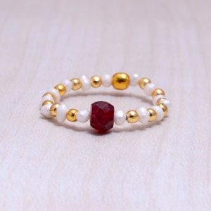 Peut inclure: Une bague composée de perles blanches et dorées avec une pierre précieuse rouge au centre.