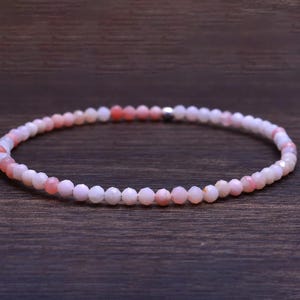 May include: A delicate pink and white opal beaded bracelet. The bracelet is made of small, faceted beads that are strung together on a clear elastic cord.