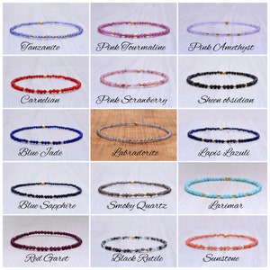 Può includere: Una collezione di delicati braccialetti con pietre preziose, ognuno con una pietra diversa e dettagli dorati. L'immagine mostra braccialetti con pietre come Tanzanite, Tormalina rosa e Corniola. Ogni braccialetto è infilato su un cordino sottile e trasparente.