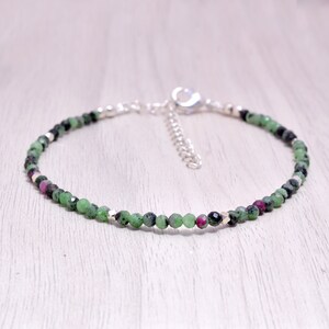 May include: A delicate bracelet made with green and pink gemstone beads and silver accents. The bracelet has a silver clasp.