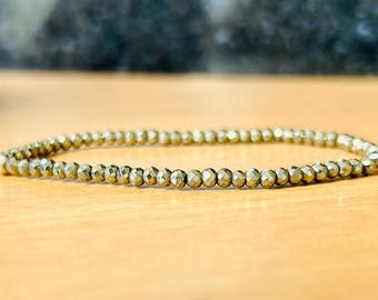 May include: A gold-toned bracelet made of small, faceted beads. The bracelet is lying on a wooden surface.